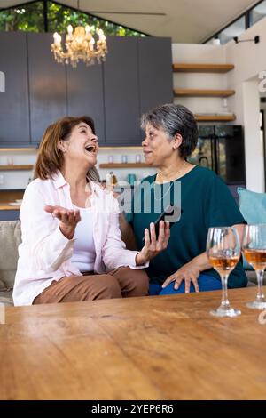 Ältere Freundinnen lachen zu Hause zusammen und genießen Gespräche mit dem Smartphone. Freunde, Bindung, Technologie, Verbindung, Glück, ältere Patienten Stockfoto