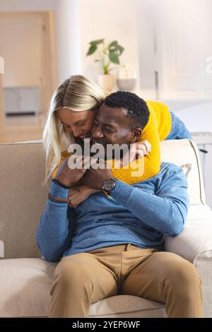 Glückliches multirassisches Paar, das sich zu Hause auf einem gemütlichen Sofa umgibt und freudige Momente miteinander teilt. Liebe, Beziehung, Romantik, Zweisamkeit, Bindung, Happes Stockfoto
