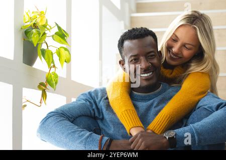 Glückliches multirassisches Paar, das sich auf Treppen umschließt und einen gemütlichen Moment zu Hause genießt. Romantisch, Beziehung, Zweisamkeit, Zuneigung, Umarmung, liebe Stockfoto