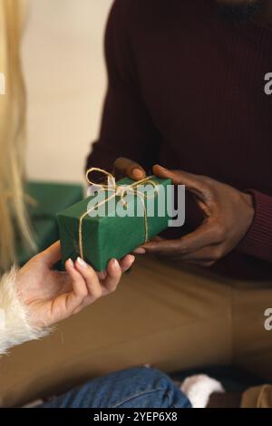 Weihnachtszeit, Geschenke austauschen, multirassisches Paar, das Urlaubsfreude teilt, zu Hause. Feiern, Geben, Festlichkeit, Zweisamkeit, Glück, Feiertagsse Stockfoto