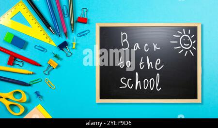 Farbenfrohe Schreibwaren umgeben eine Tafel, auf der der Satz zurück zur Schule vor einem hellblauen Hintergrund dargestellt wird. Stockfoto