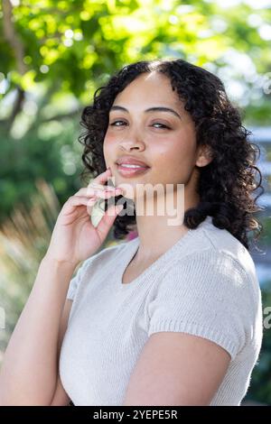 Lächelnde Frau, die sonnigen Tag im Freien genießt, umgeben von üppigem Grün. Natur, Glück, Freizeit, Entspannung, Sommer, Freiheit Stockfoto