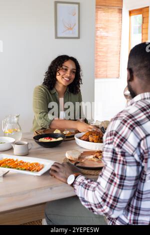 Ein lächelndes multirassisches Paar genießt zu Hause ein Thanksgiving-Dinner und teilt das Essen. Feier, Familie, Urlaub, fest, Tradition, Festmahl Stockfoto
