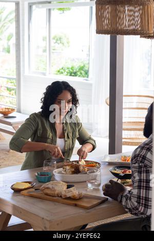 Lächelnde Frau schnitzt truthahn zu Hause und genießt Thanksgiving-Mahlzeit mit Partner. Feiern, Essen, festlich, Urlaub, Zweisamkeit, kulinarisch Stockfoto