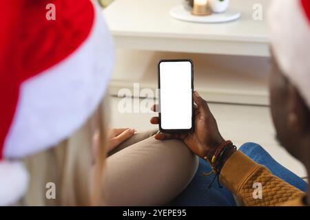Weihnachten, multirassisches Paar, das zu Hause auf den Smartphone-Bildschirm schaut, im Kopierraum, zu Hause. Familie, weihnachten, Urlaub, Zweisamkeit, Technologie, CE Stockfoto