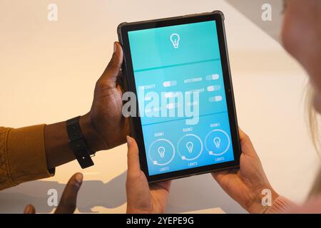 Multiethnische Paare verwenden ein Tablet, um das intelligente Beleuchtungssystem gemeinsam zu steuern. Technologie, Innovation, Automatisierung, Komfort, Lifestyle, Connectivi Stockfoto