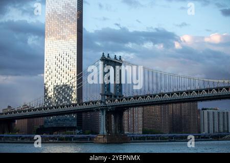 Bild mit der Manhattan Bridge über den East River mit einem hohen, reflektierenden Wolkenkratzer im Hintergrund. Stockfoto