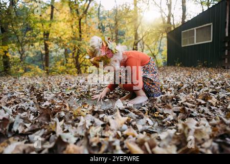 Kind in skurriler Herbstkleidung, das in Blättern spielt Stockfoto