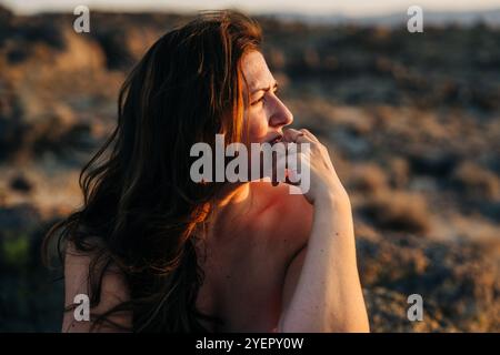 Nachdenkliche Frau, die in warmem Abendlicht in die Ferne schaut Stockfoto