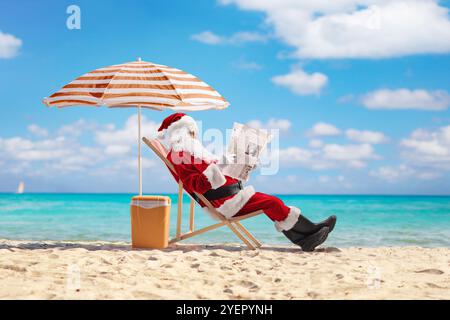 Der weihnachtsmann liest eine Zeitung und sitzt auf einem Liegestuhl am Meer Stockfoto