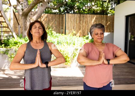 Ältere Freundinnen üben Yoga im Freien, meditieren mit geschlossenen Augen, fühlen sich friedlich. Meditation, Entspannung, Wellness, Ruhe, achtsam Stockfoto