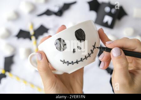 Weibliche Hände malen auf weißem Becher unheimlich Jacks Gesicht DIY für Kinder Halloween Home Aktivitäten Holiday Art Kinder Handwerk handgefertigte Dekorationen. Schritt für Schritt Stockfoto