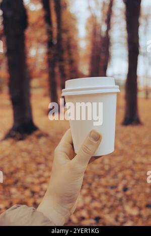 Unerkennbare Frau mit Eco Zero Waste White Paper Cup Copy Space Mockup. Herbstblätter und eine Tasse Tee und Kaffee, um in die herbstliche Natur zu gehen. Uni Stockfoto