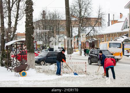 Romny, Ukraine, 2. Februar 2021: Arbeiter mit Schaufeln reinigen den Gehweg, entfernen Schnee und schmelzendes Eis in einer Winterstadt Stockfoto