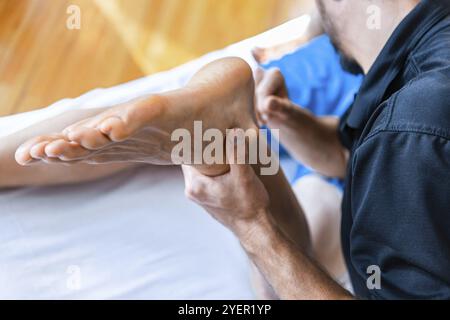 Junger Mann mit Fußmassage. Nahaufnahme der Masseurarme, die eine Massage an einen starken männlichen Patienten durchführen. Sportmassage Stockfoto