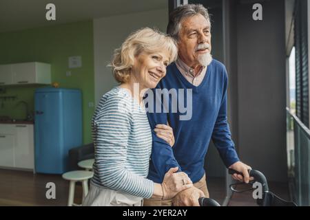 Seniorenpaar, das aus dem Fenster schaut, während er sich umarmt Stockfoto