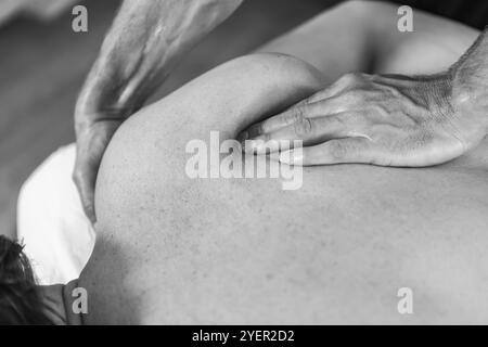 Schwarz-Weiß-Bild von professionellen Masseur-Therapeuten-Händen, die eine Massage geben. Nahaufnahme des jungen Sportlers, der eine Rückenmassage erhält Stockfoto