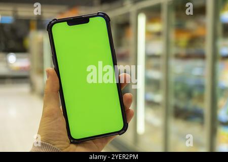 Chroma-Taste für Mobiltelefone auf dem Hintergrund von Unschärfe-Effekte im Tiefkühlschrank. Nahaufnahme einer Frau hält Smartphone mit grünem Bildschirm im Einkaufszentrum. Stockfoto