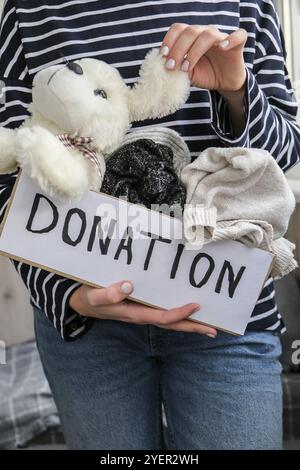 Weibliche Freiwillige hält Spendenbox mit alten gebrauchten Spielsachen und Kleidung in Innenräumen. Frohe Charity. Unkenntlich Frau, die Box mit Kleidung darin hält. clos Stockfoto