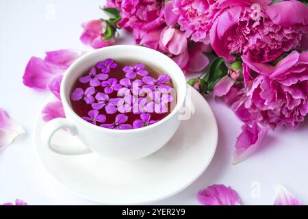 Kreatives Layout mit pinkfarbenen Pfingstrosen-Blumen und einer Tasse Tee auf einem hellen Tisch. Frühling saisonal valentinstag, Frau, Mutter, 8 märz Urlaub, Romantik-Frühstück Stockfoto