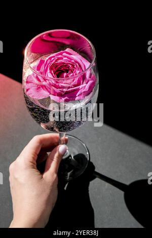 Weinglas mit rosa Blume Petalson Tisch mit schwarzen gefüllt. Minimales modernes Stillleben. Urlaubskonzept Valentinstag- oder Frauentag im Hintergrund. C Stockfoto