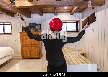 Rückansicht einer Bauinspektorin mit rotem Schutzhelm. Sie hebt die Hände hoch, während sie ein Klemmbrett und eine Wasserwaage hält Stockfoto