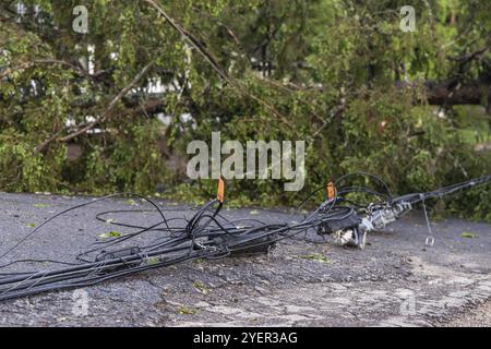 Nahaufnahme selektiver Fokus auf gefährliche Stromversorgungsdrähte, die auf der Asphaltfläche der Hauptstraße liegen, nachdem starke Winde die Oberleitungen niederreißen Stockfoto