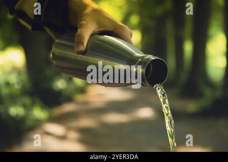 Nahaufnahme einer nicht erkennbaren Wasserflasche mit der Hand. Gießen von sauberem Wasser Wiederverwendbare Wärmflasche aus Stahl im Park. Nachhaltiger Lebensstil. Pl Stockfoto