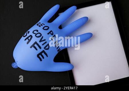 Aufgeblasene blaue Latex-OP-Handschuh auf schwarzem Hintergrund. Erneutes Öffnen von covid Safe. Öffnen Sie wieder Text auf medizinischen Handschuh geschrieben. Neuer Normalwert. Coronavirus outbre Stockfoto