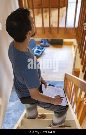 Eine Nahaufnahme und Hochwinkelansicht eines kaukasiers, der während der Hauseinkäuferkontrolle auf einer Treppe steht und strukturelle Qualitäten und Probleme überprüft Stockfoto