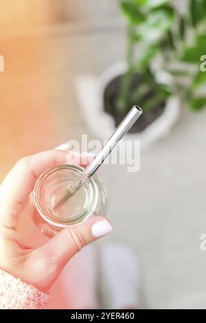 Draufsicht weibliches Hand-Trinkwasser aus Öko-Flasche mit wiederverwendbarem Metallstrohrohr. Achtsamkeitsmeditation. Das Konzept der gesunden Ernährung, Umwelt Stockfoto