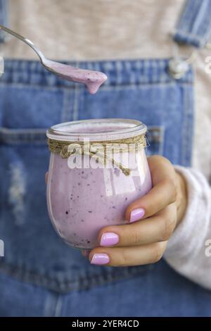 Weibliche Hände halten Blueberry Smoothie mit Heidelbeeren gekrönt. Frau, die ein Glas Frühstücksprotein-Smoothie-Getränk aus pürierten rohen Blauberri isst Stockfoto