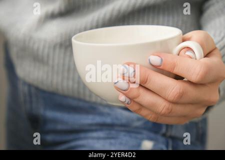 Gepflegte weibliche Hände halten weiße Kaffeetasse mit stilvollen blauen Nägeln und minimalistischem Design. Trendige Maniküre in modernem Design. Gelnägel. Hautpflege. Stockfoto