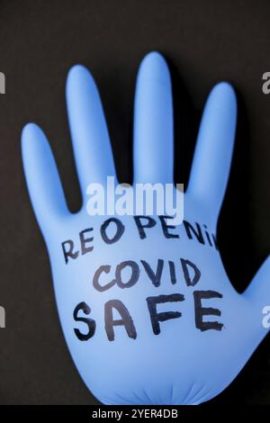 Aufgeblasene blaue Latex-OP-Handschuh auf schwarzem Hintergrund. Erneutes Öffnen von covid Safe. Öffnen Sie wieder Text auf medizinischen Handschuh geschrieben. Neuer Normalwert. Coronavirus outbre Stockfoto