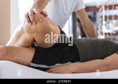 Ein Sportler, der eine medizinische Beinmassage erhält. Ein junger Mann, der auf dem Massagettisch liegt und eine behandelnde Beinmassage im medizinischen Zentrum hat Stockfoto