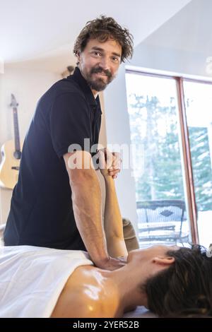 Vertikaler Schuss der jungen Frau, die auf einem Massagetisch liegt und in gemütlicher Hausumgebung Handmassage und spezielle Akupressur bekommt Stockfoto