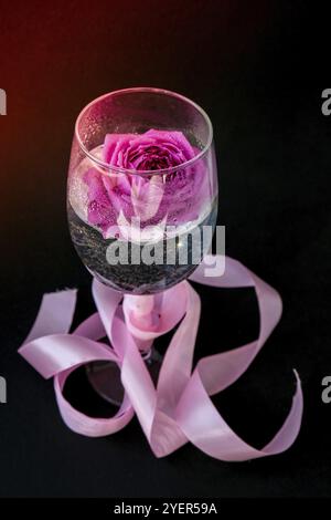 Weinglas mit rosa Blume Petalson Tisch mit schwarzen gefüllt. Minimales modernes Stillleben. Urlaubskonzept Valentinstag- oder Frauentag im Hintergrund. C Stockfoto