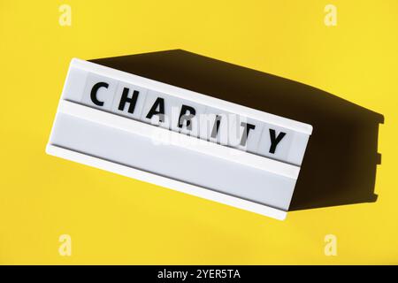 Leuchtkasten mit Text CHARITY. Motivationswörter Zitate Konzept. Farbenfroher gelber Hintergrund. Minimalistisches kreatives Konzept. Spendenunterstützung Stockfoto