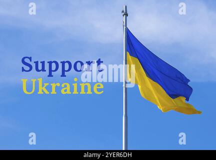 UNTERSTÜTZE den UKRAINISCHEN Text über die ukrainische Nationalflagge flattert im Wind gegen den blauen Himmel. Nationales Symbol des ukrainischen Volkes, blau und gelb. Indep Stockfoto