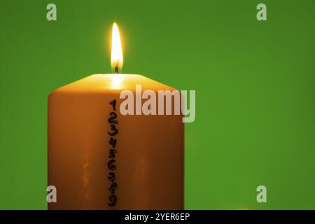 Kerze mit Adventskalender auf grünem Chroma-Schlüsselhintergrund traditionelle brennende Weihnachtswachskerzen mit Zahlen, die für Weihnachten herunterzählen. Schön Stockfoto