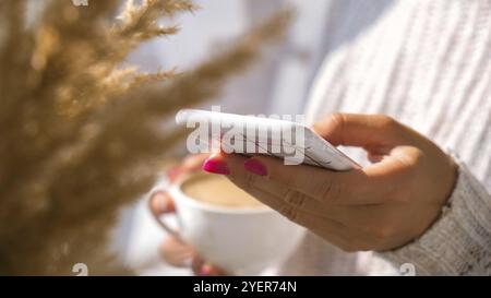 Frau mit Mobiltelefon. Pampas Gras Heimtextilien. Beim Cappuccino am Morgen zu Hause soziale Medien checken. Ästhetik Stockfoto