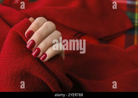 Frau gepflegte Hände, stilvolle rote Nägel, Copy Space. Roter Pullover Closeup. Design-Konzept im Winter- oder Herbststil. Schönheitsbehandlung. Fallnägel Stockfoto