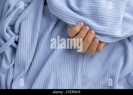 Frau hat die Hände gepflegt, stilvolle beige Nägel. Die Nahaufnahme von gepflegten Nägeln der weiblichen Hand in blauem Pullover auf blauem Hintergrund. Winter- oder Herbststil Stockfoto