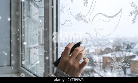 Weibliche Hand Malerei Weihnachtshirsch auf Fensterglas gemalt. Weihnachtliche Winterdekoration auf dem Fensterglas. Weißes Muster von Hirschen. Snow Art Tracery Windo Stockfoto