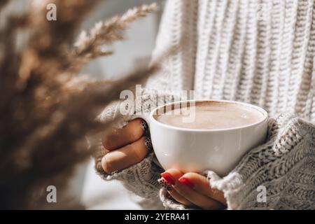 Pampas Gras und weibliche Hand halten weiße Tasse mit Kaffee. Trinken Cappuccino am Morgen Frühstück zu Hause. Ästhetik. Gemütliches Zuhause Stockfoto