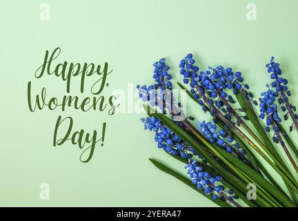 HAPPY WOMEN DAY Postkarte Layout. Frühling modernes Stillleben. Blaue Muscari-Blüten, die aus rechteckigem, in Papier geschnittenem Papier auf blauem Hintergrund wachsen. Minimale Spr Stockfoto