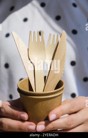 Weibliche Hände mit Holzgabeln und Pappbecher mit Tellern. Umweltfreundliches Einweggeschirr. Wird in Fast Food, Restaurants, Imbissbuden und Picknicks verwendet. N Stockfoto