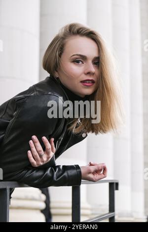 Porträt einer jungen blonden Frau mit roten Lippen in Lederjacke auf der Treppe des Firmengebäudes. Karriere Geschäftsfrau. Stylische Biker-Frau. Urban Street Stockfoto