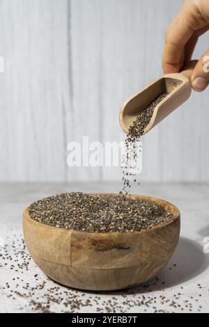 Chiasamen fallen in eine Holzschüssel. Gesundes Superfood reich an Omega 3 Fettsäuren. Trockene gesunde natürliche Zutat. Chia-Körner fallen. Vegetarischer Foo Stockfoto