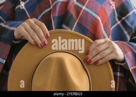 Stylische rote Frauennägel. Frau in Poncho mit braunem trendigen Hut. Moderne, wunderschöne Maniküre. Herbst Winter Nagel Design Konzept der Beauty-Behandlung. Stockfoto